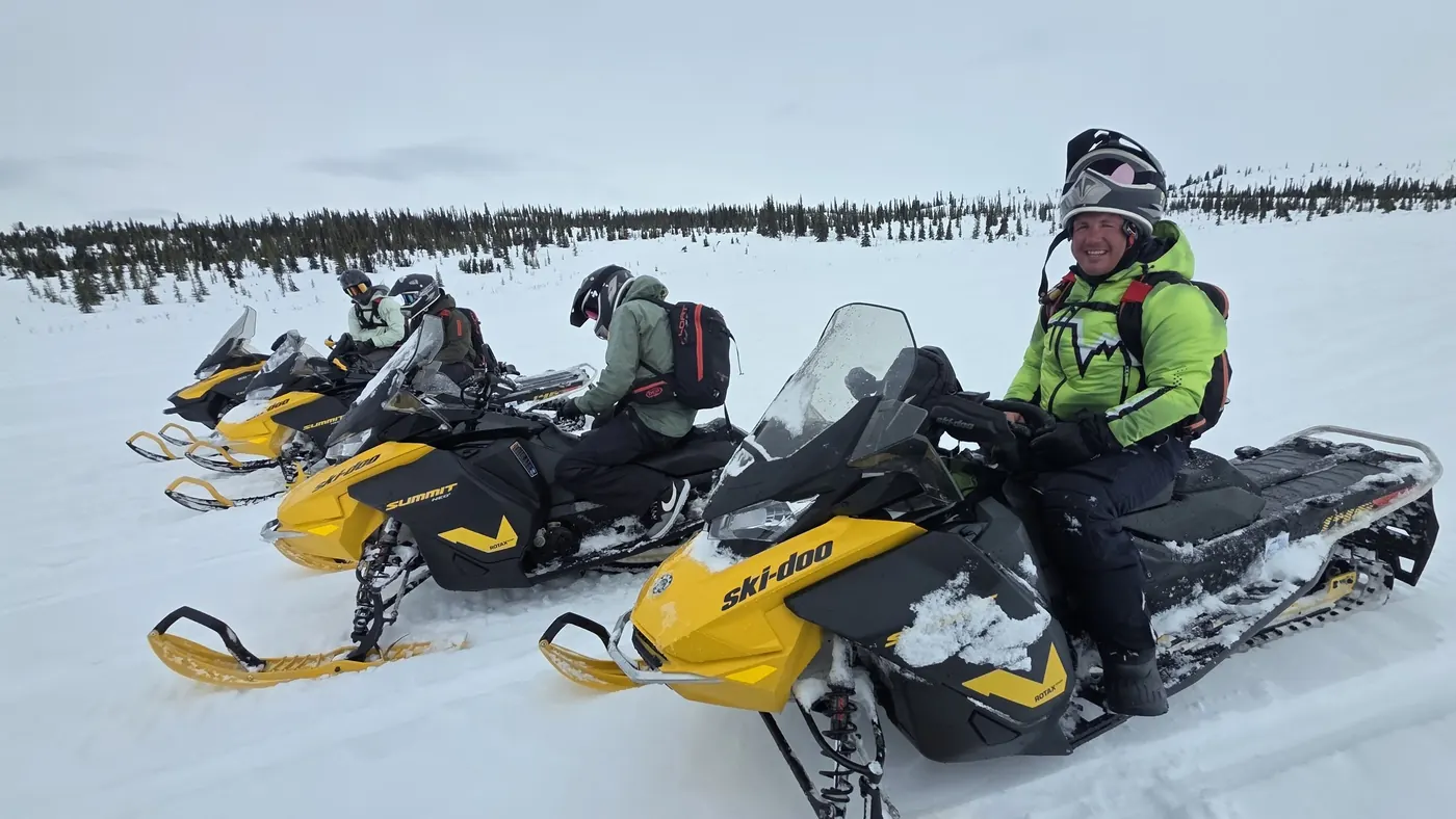 A line of yellow snowmobiles with riders ready to set off across open snow